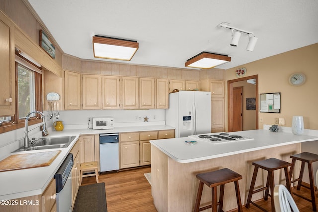 kitchen with light brown cabinetry, a sink, white appliances, a kitchen breakfast bar, and a peninsula