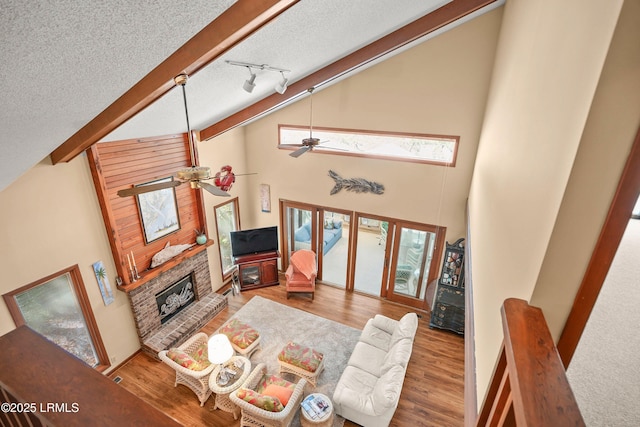 living area with a ceiling fan, a textured ceiling, a brick fireplace, wood finished floors, and high vaulted ceiling