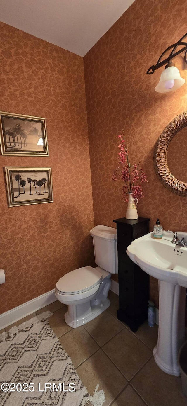 half bathroom with toilet, tile patterned flooring, and baseboards