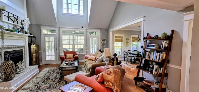 living room with wood finished floors, a fireplace with raised hearth, healthy amount of natural light, and high vaulted ceiling