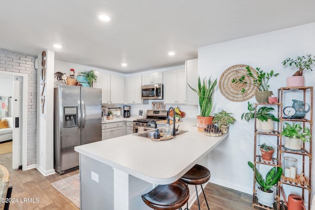 kitchen with a breakfast bar, appliances with stainless steel finishes, kitchen peninsula, and light hardwood / wood-style floors