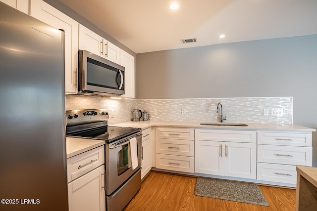 1348 Rowland Dr, Saint Helena Island, SC 29920 - kitchen with sink, white cabinetry, light wood-type flooring, stainless steel appliances, and backsplash