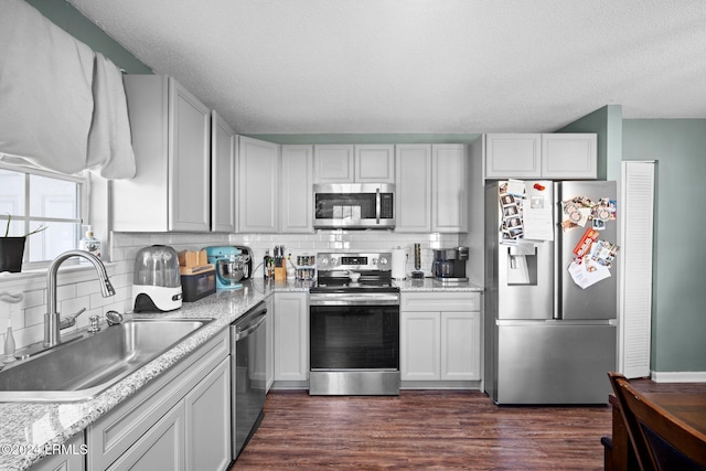 kitchen with sink, appliances with stainless steel finishes, tasteful backsplash, white cabinets, and dark hardwood / wood-style flooring