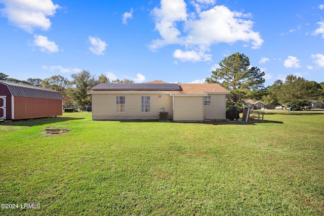 rear view of property with solar panels, central AC unit, a lawn, a fire pit, and a shed