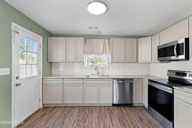 kitchen with stainless steel appliances, white cabinetry, sink, and light wood-type flooring