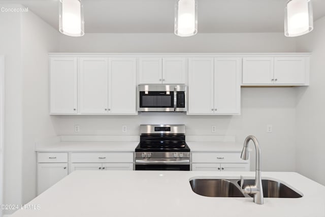 kitchen with white cabinetry, stainless steel appliances, decorative light fixtures, and sink