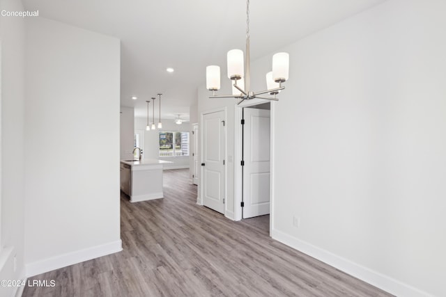 unfurnished dining area featuring an inviting chandelier, sink, and light hardwood / wood-style flooring