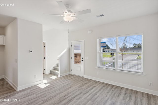 unfurnished living room featuring light wood finished floors, baseboards, visible vents, ceiling fan, and stairs