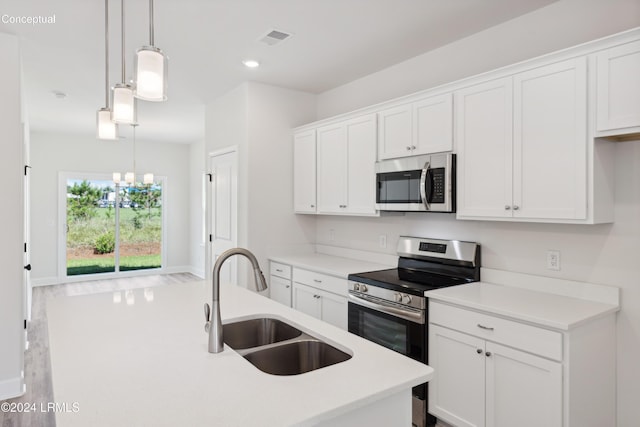 kitchen featuring sink, white cabinetry, hanging light fixtures, stainless steel appliances, and an island with sink