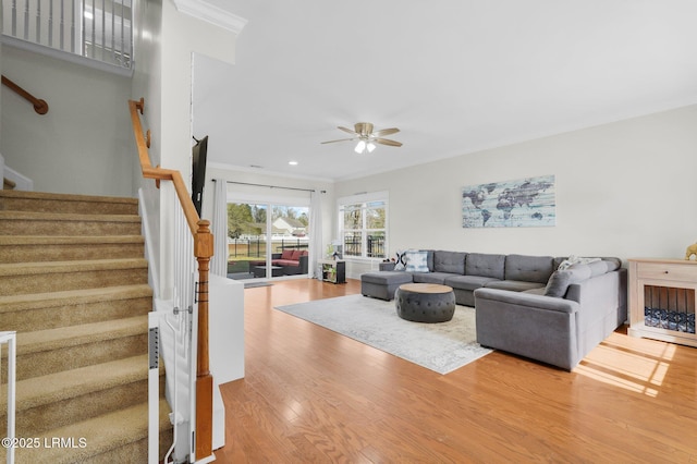 living area with wood finished floors, stairway, a ceiling fan, and ornamental molding