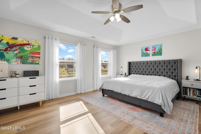 bedroom with light wood finished floors, visible vents, ceiling fan, baseboards, and a tray ceiling