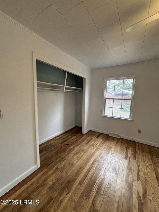 unfurnished bedroom with a closet, visible vents, baseboards, and wood finished floors