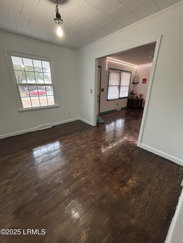 empty room featuring a healthy amount of sunlight, dark wood-style floors, visible vents, and ornamental molding