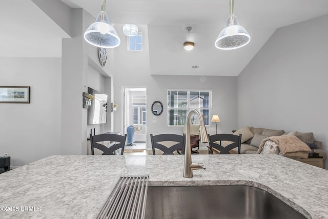 kitchen with vaulted ceiling, light stone countertops, a wealth of natural light, and pendant lighting