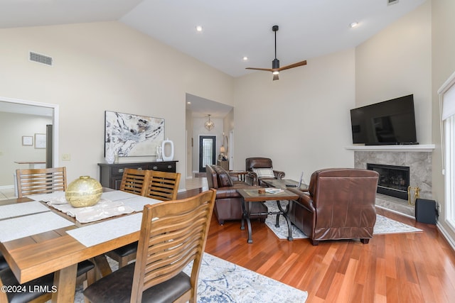 dining room with hardwood / wood-style floors, a fireplace, high vaulted ceiling, and ceiling fan