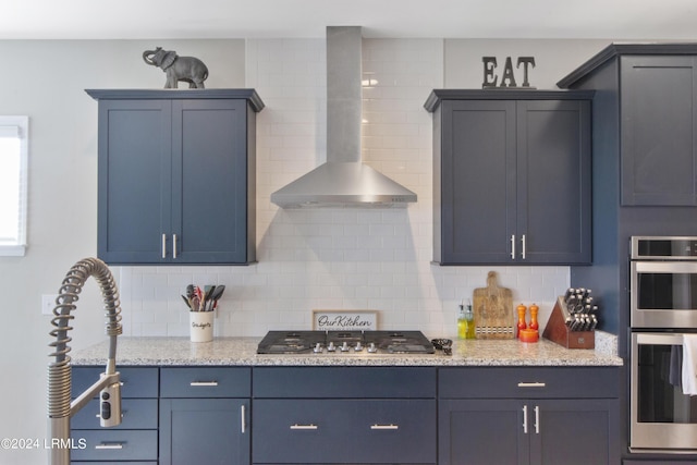 kitchen with appliances with stainless steel finishes, blue cabinetry, decorative backsplash, and wall chimney exhaust hood