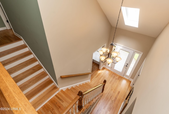 stairs featuring an inviting chandelier, wood-type flooring, and high vaulted ceiling