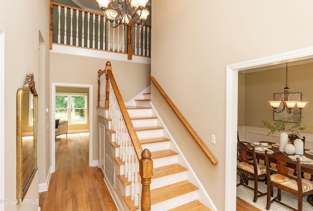 stairs with a towering ceiling, wood-type flooring, and a chandelier