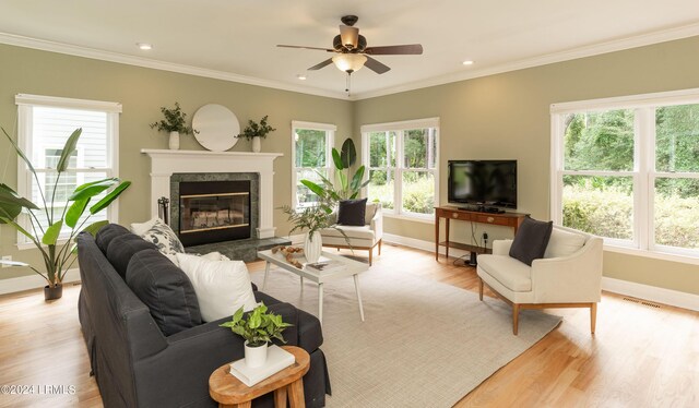 living room featuring a premium fireplace, ornamental molding, ceiling fan, and light hardwood / wood-style floors