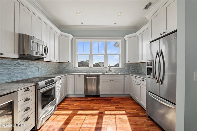 kitchen with crown molding, stainless steel appliances, visible vents, a sink, and light stone countertops