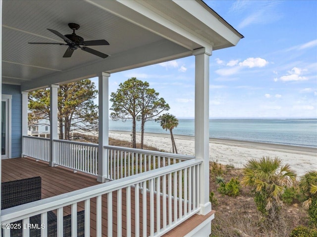 wooden deck with a water view, a view of the beach, and a ceiling fan