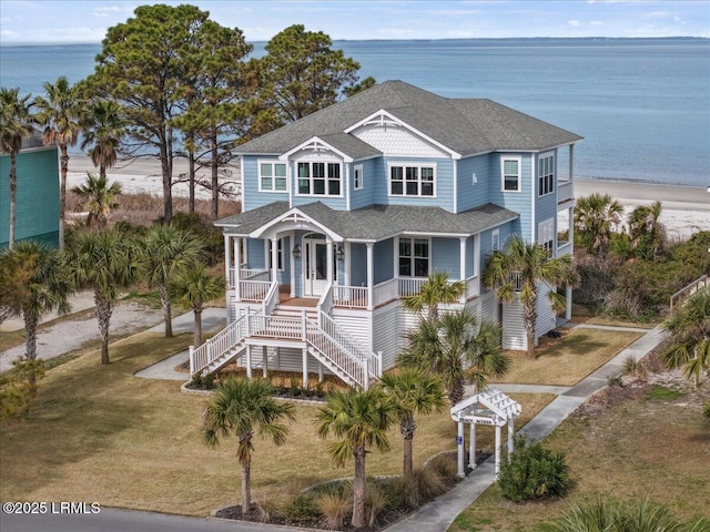 coastal home featuring a shingled roof, a water view, stairs, a porch, and a front yard