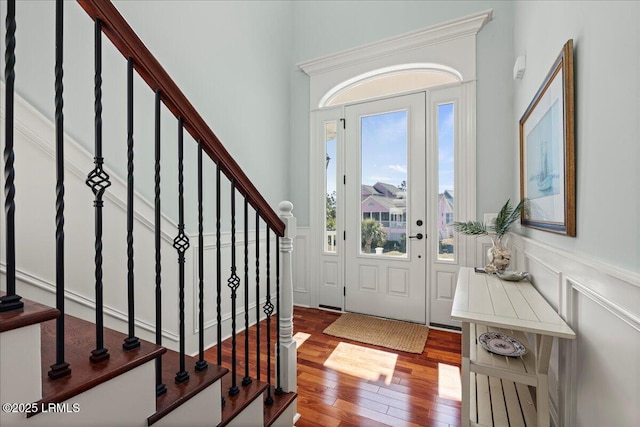 entrance foyer with wood-type flooring, stairway, a decorative wall, and wainscoting