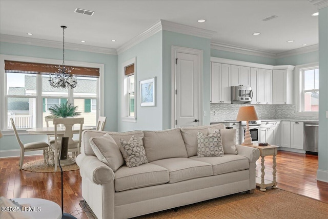 living area with a chandelier, ornamental molding, light wood-type flooring, and visible vents