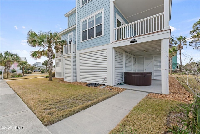 view of property exterior featuring a balcony, a hot tub, and a lawn