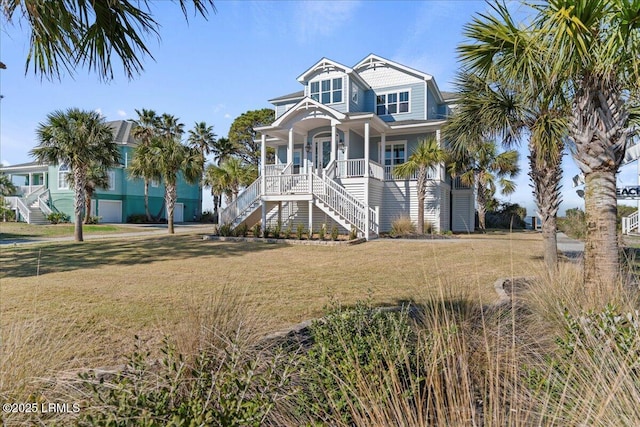 raised beach house featuring covered porch, stairway, and a front yard