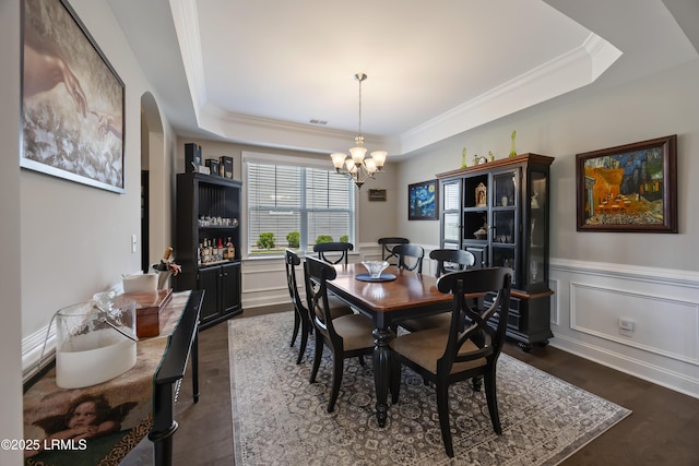 dining space with a chandelier, dark wood-style floors, crown molding, a tray ceiling, and wainscoting