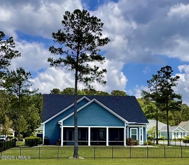 rear view of house featuring a shingled roof, a sunroom, a lawn, and a fenced front yard