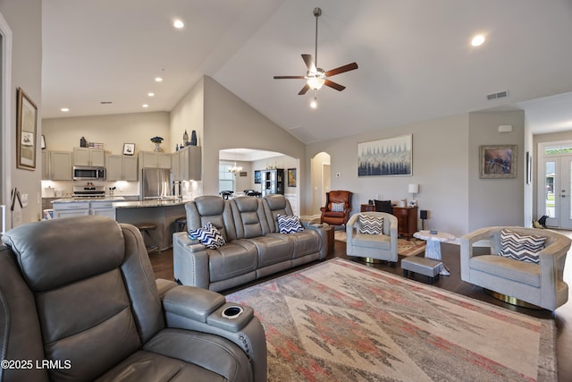 living area with ceiling fan with notable chandelier, high vaulted ceiling, arched walkways, visible vents, and wood finished floors