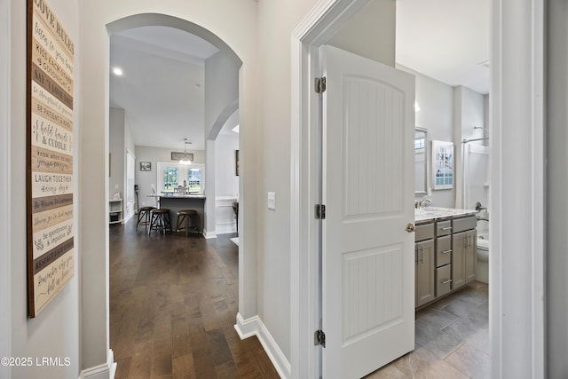 hall with dark wood-type flooring, arched walkways, a sink, and baseboards