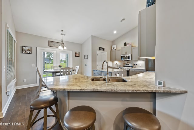 kitchen with a peninsula, appliances with stainless steel finishes, light stone counters, a sink, and a breakfast bar area