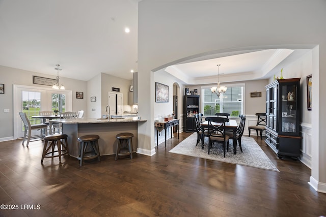 dining area featuring a chandelier, arched walkways, dark wood-style flooring, and a healthy amount of sunlight