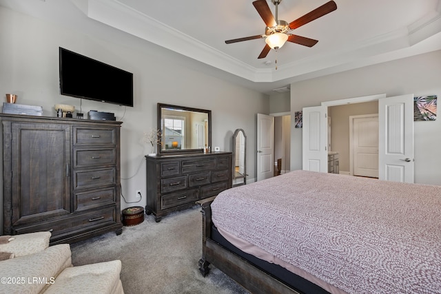 carpeted bedroom with a tray ceiling, crown molding, and ceiling fan