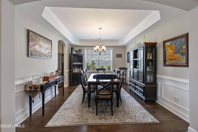 dining space featuring a notable chandelier, dark wood-style floors, a tray ceiling, a decorative wall, and arched walkways