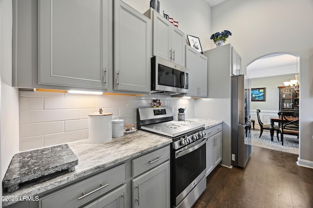 kitchen with gray cabinets, appliances with stainless steel finishes, arched walkways, and dark wood-style floors