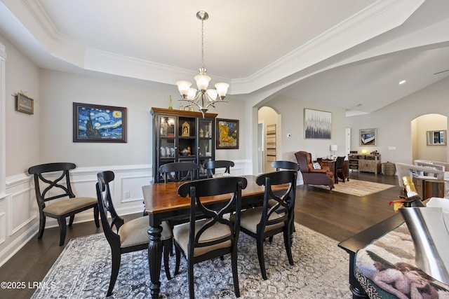 dining space featuring a wainscoted wall, arched walkways, a notable chandelier, and dark wood finished floors