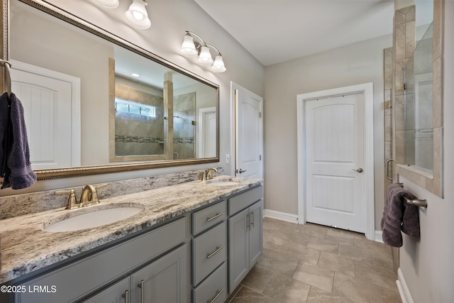 bathroom with a shower stall, double vanity, baseboards, and a sink