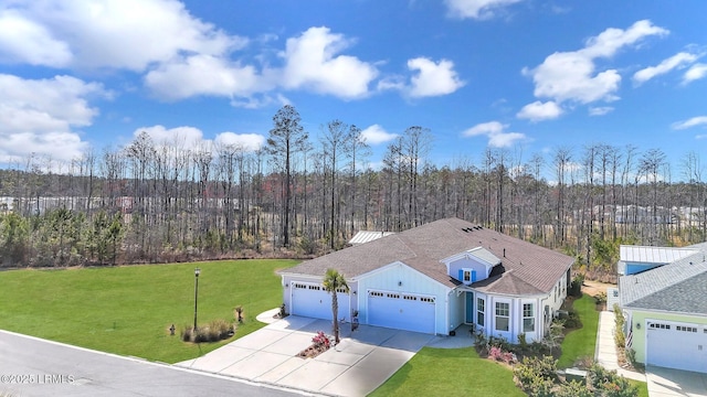 view of front of home with a garage, driveway, roof with shingles, a front lawn, and a wooded view