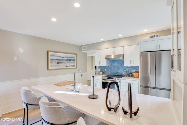 kitchen featuring sink, a breakfast bar area, appliances with stainless steel finishes, white cabinetry, and light hardwood / wood-style floors