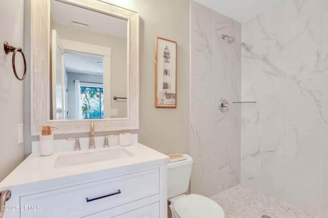 bathroom with tiled shower, vanity, and toilet