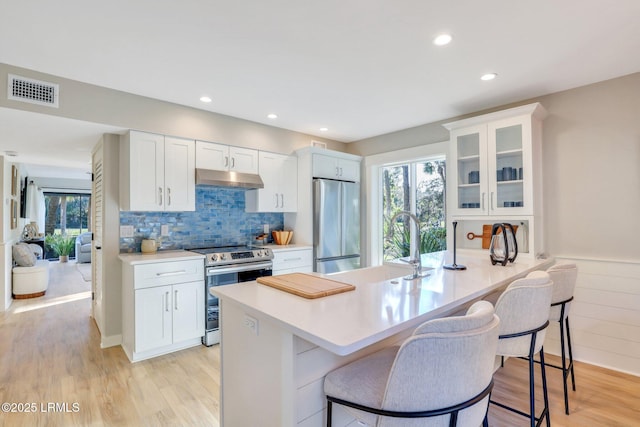 kitchen with light hardwood / wood-style flooring, stainless steel appliances, white cabinets, and a kitchen bar