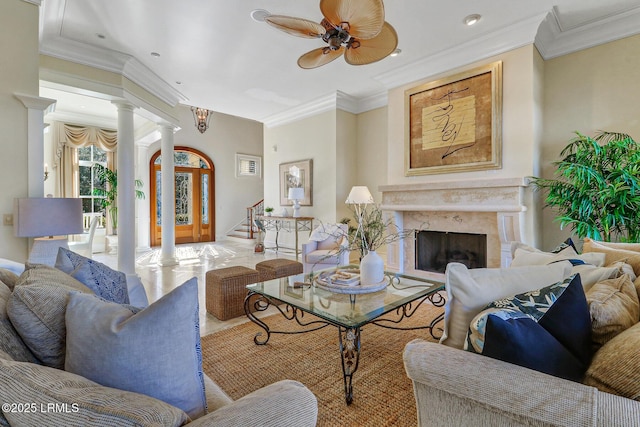 living room featuring crown molding, decorative columns, stairway, a premium fireplace, and a ceiling fan