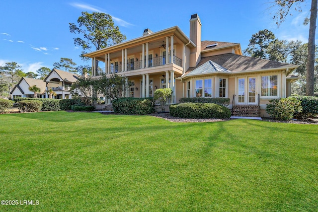 back of property with a chimney, stucco siding, a lawn, ceiling fan, and a balcony