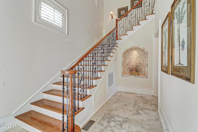 stairs featuring marble finish floor, a towering ceiling, visible vents, and baseboards