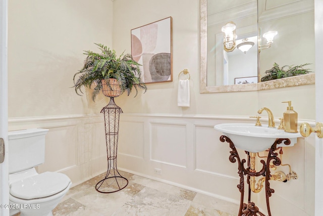 half bathroom with a wainscoted wall, a decorative wall, and toilet