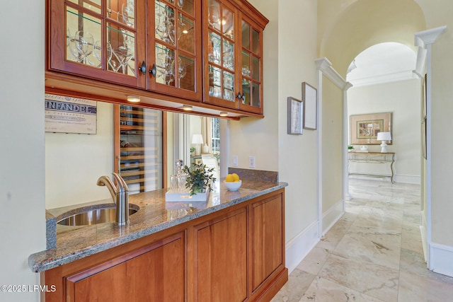 bar with arched walkways, a sink, baseboards, marble finish floor, and ornate columns